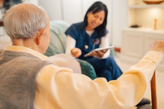 Rear view of a elderly man and female caregiver during a home visit